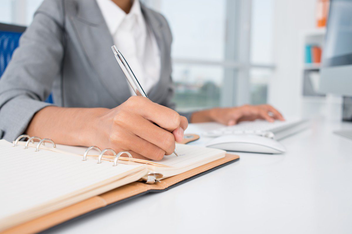 GettyImages-178609380 Person writing in notebook at desk.