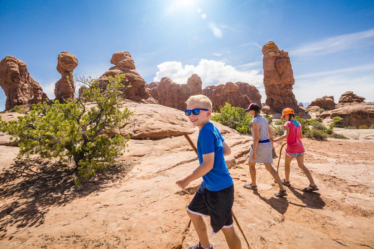 GettyImages-935877230 Family hiking in sunny desert landscape.