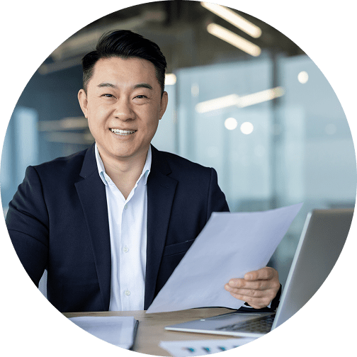 GettyImages-2187323050 Smiling man holding papers at office desk.