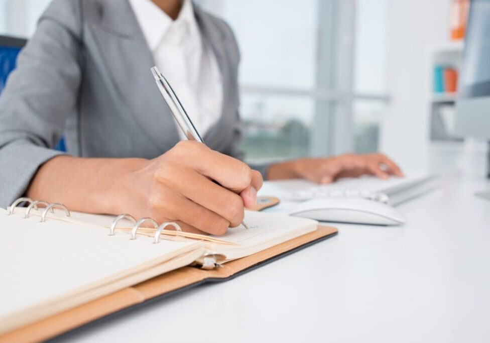 Person writing in notebook at desk.